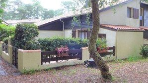 Uma casa com telhado de azulejos, cerca de madeira e plantas em vasos.
