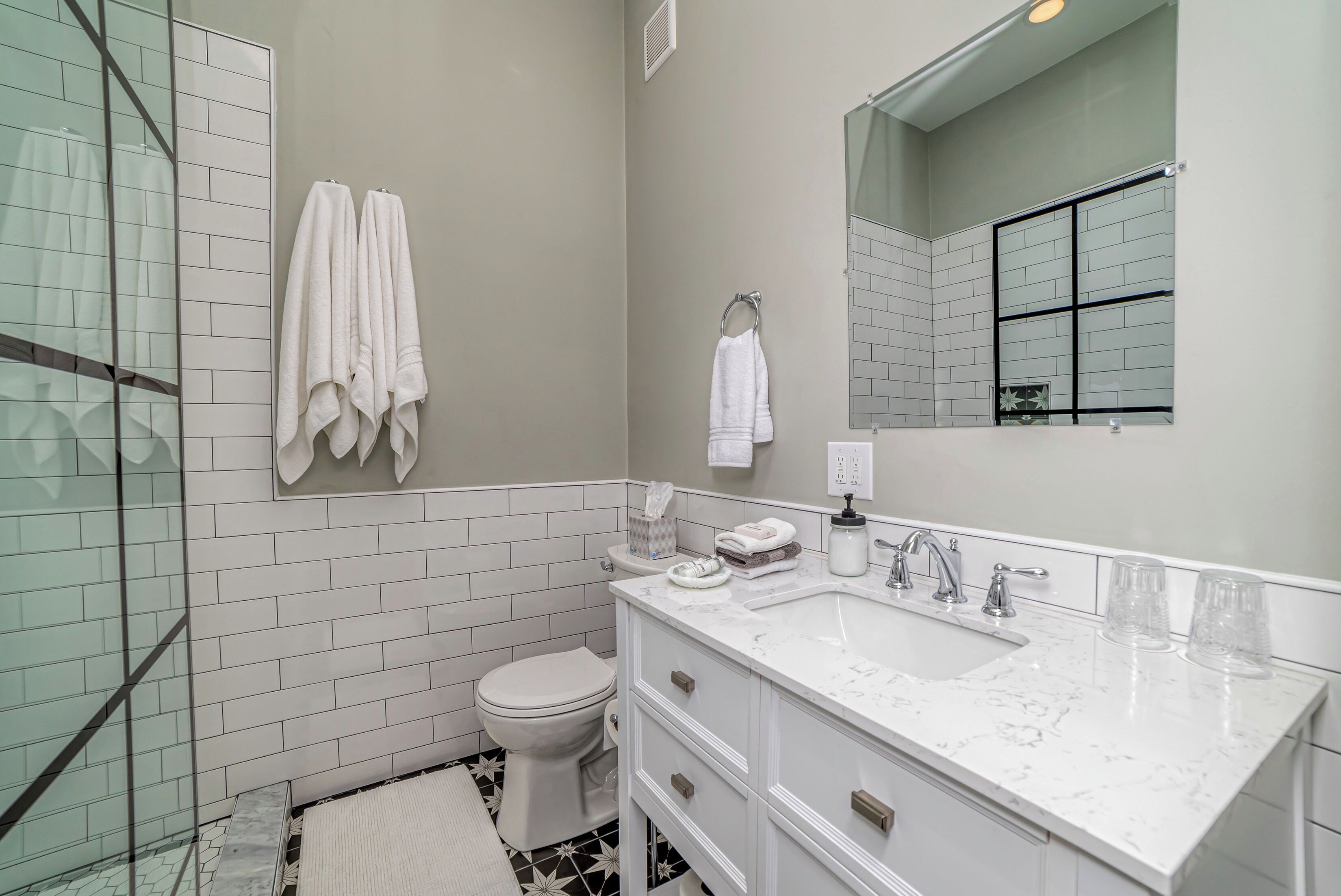 A modern bathroom with a glass shower enclosure, white tiled walls, a white sink with a marble countertop, and a toilet.