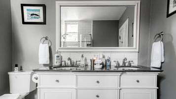 A bathroom with a large mirror, two sinks, white cabinets, and a toilet.