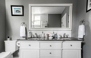A bathroom with a large mirror, two sinks, white cabinets, and a toilet.