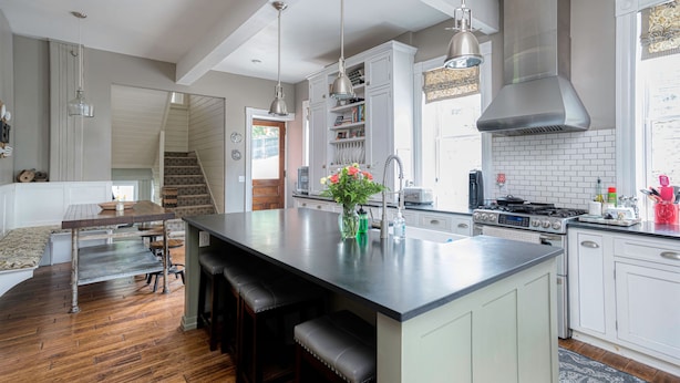 Une cuisine moderne dotée d’un grand îlot central, de meubles blancs, d’appareils électroménagers en acier inoxydable et d’un plancher en bois.