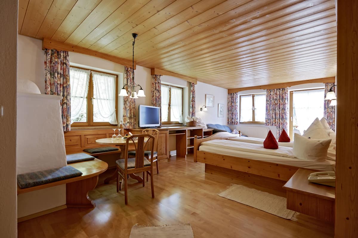 Ein gemütliches Blockhauszimmer mit Holzbalkendecke, einem Bett mit Kissen, einem Schreibtisch mit Computer, einem Stuhl und einem Fenster mit Vorhängen.
