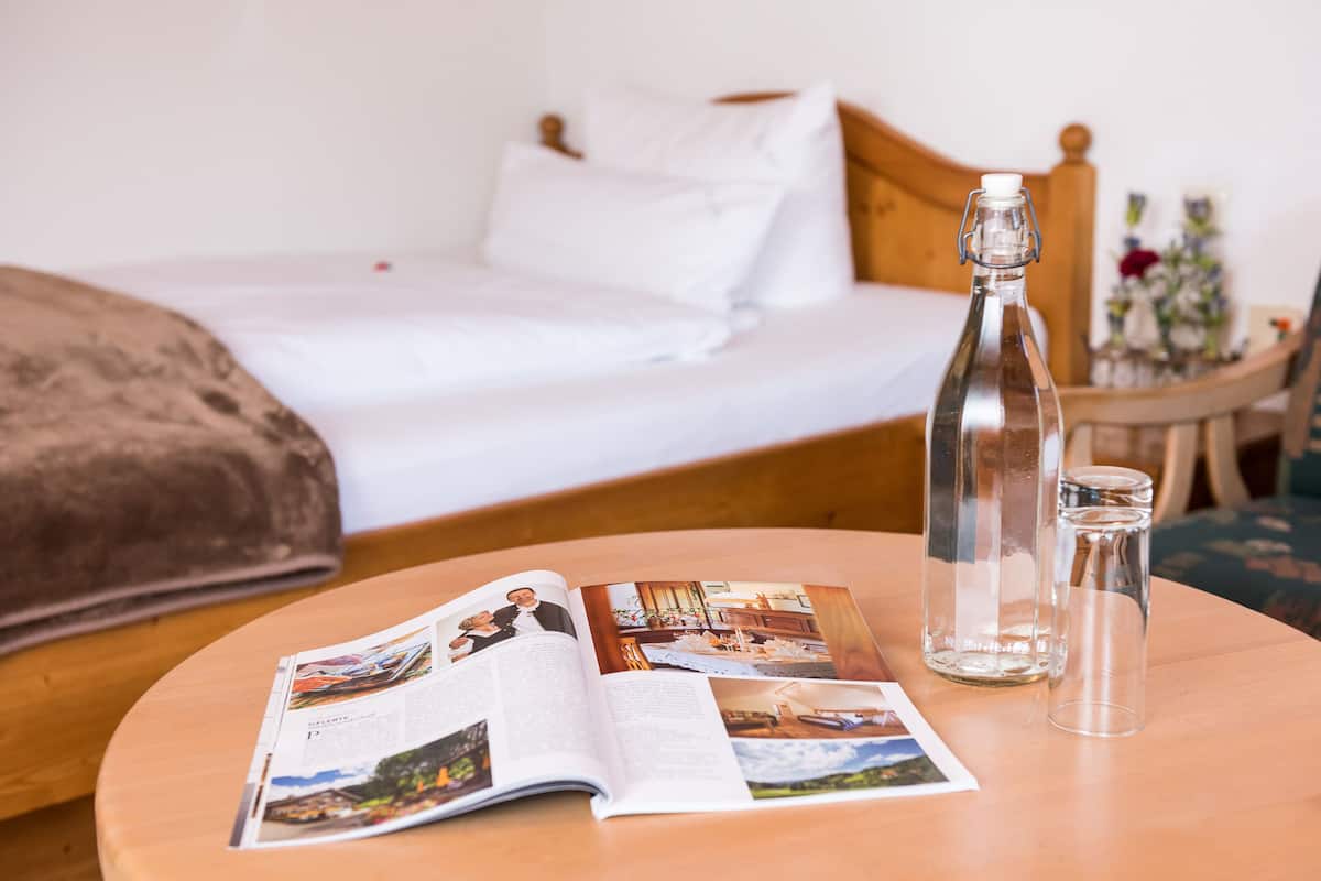 Ein Hotelzimmer mit einem Bett, einem runden Holztisch mit einer Zeitschrift, einer Glasflasche und einem Glas.