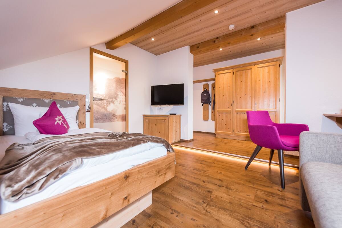 Ein Schlafzimmer mit einem Holzbett, einem Fernseher, einem Kleiderschrank und einem Sessel.