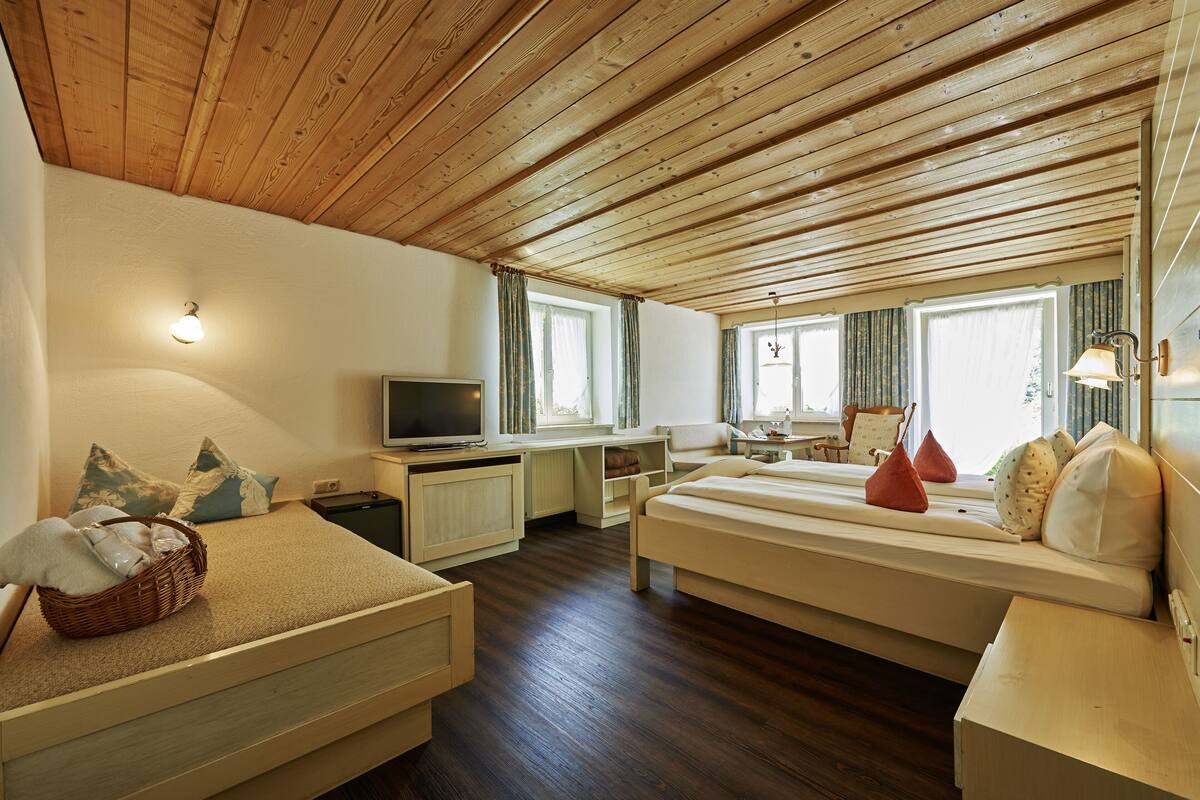 Ein gemütliches Zimmer mit Holzbalkendecke, einem Bett, einem Schreibtisch und einem Fernseher.