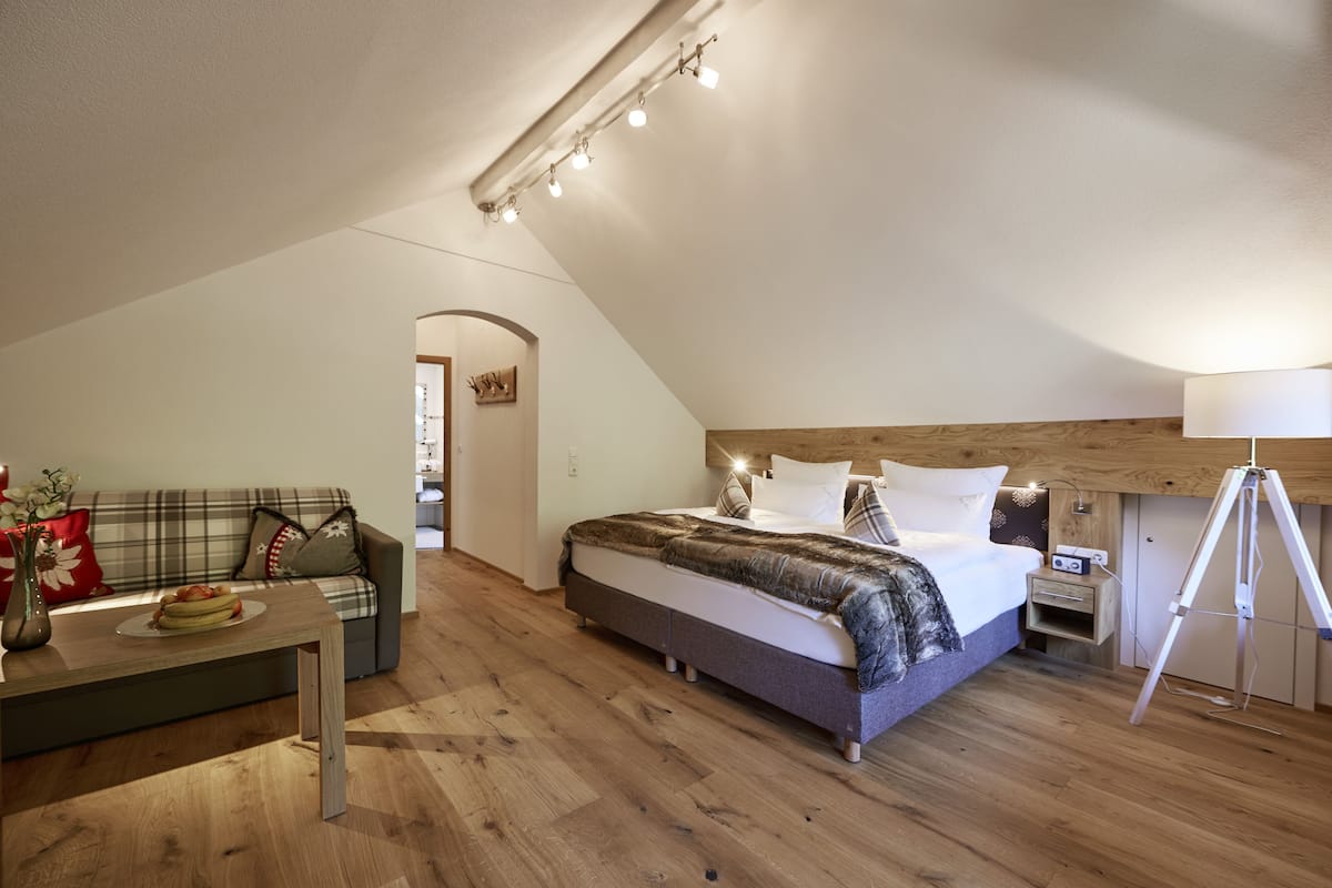 Ein Schlafzimmer mit einem Bett, Holzboden, einer Couch, einem Tisch mit einer Vase und einer Lampe.