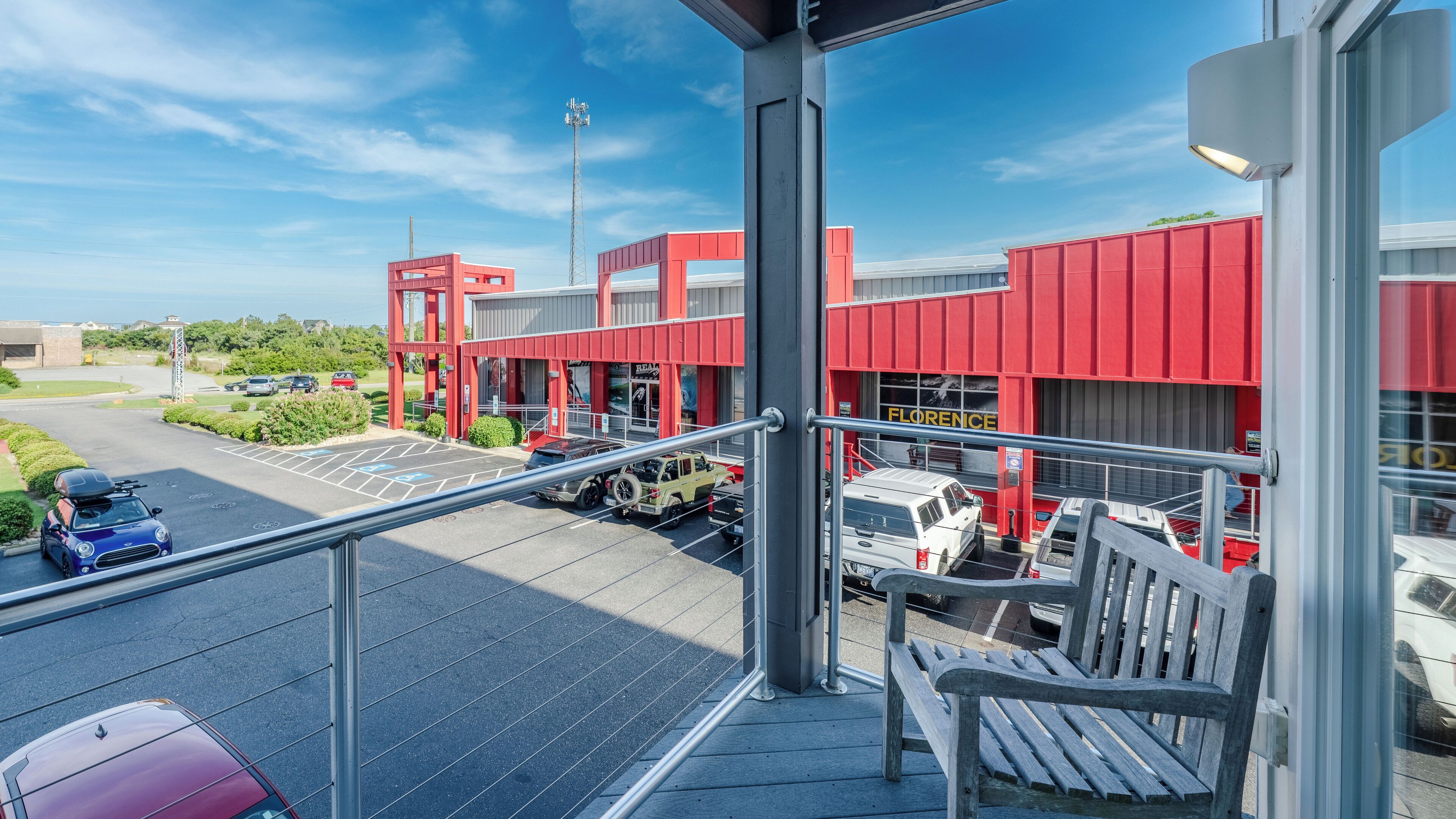 A view from a balcony overlooking a parking area with several vehicles, including a white van and a red truck, and a building with a red facade and the word "FLORENCE" on it.