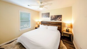 A neatly arranged bedroom with a large bed, two bedside tables with lamps, a ceiling fan, and artwork on the wall.