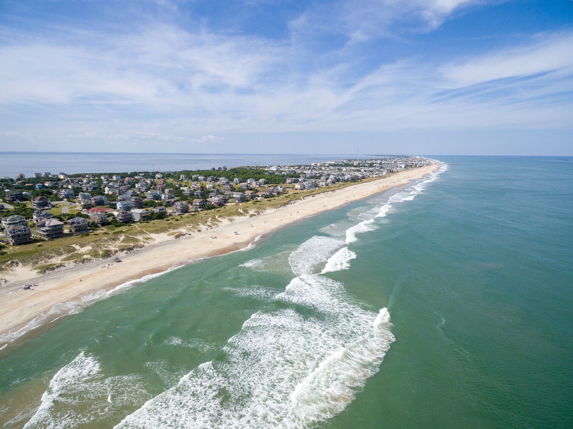 An aerial view of a coastal residential area with houses along the beach and ocean waves.