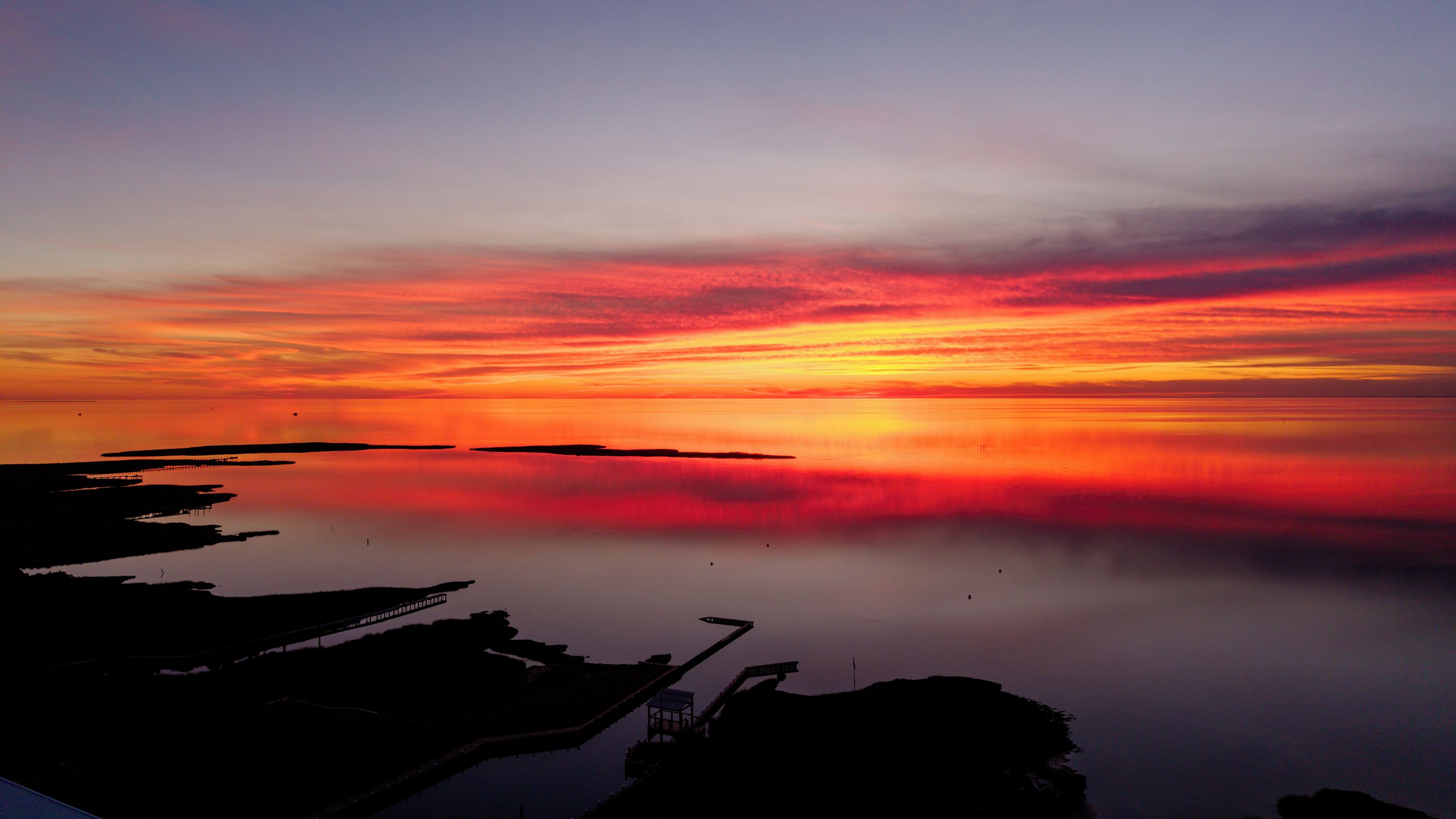 Un coucher de soleil sur une étendue d’eau calme, avec une jetée qui s’avance dans l’eau.