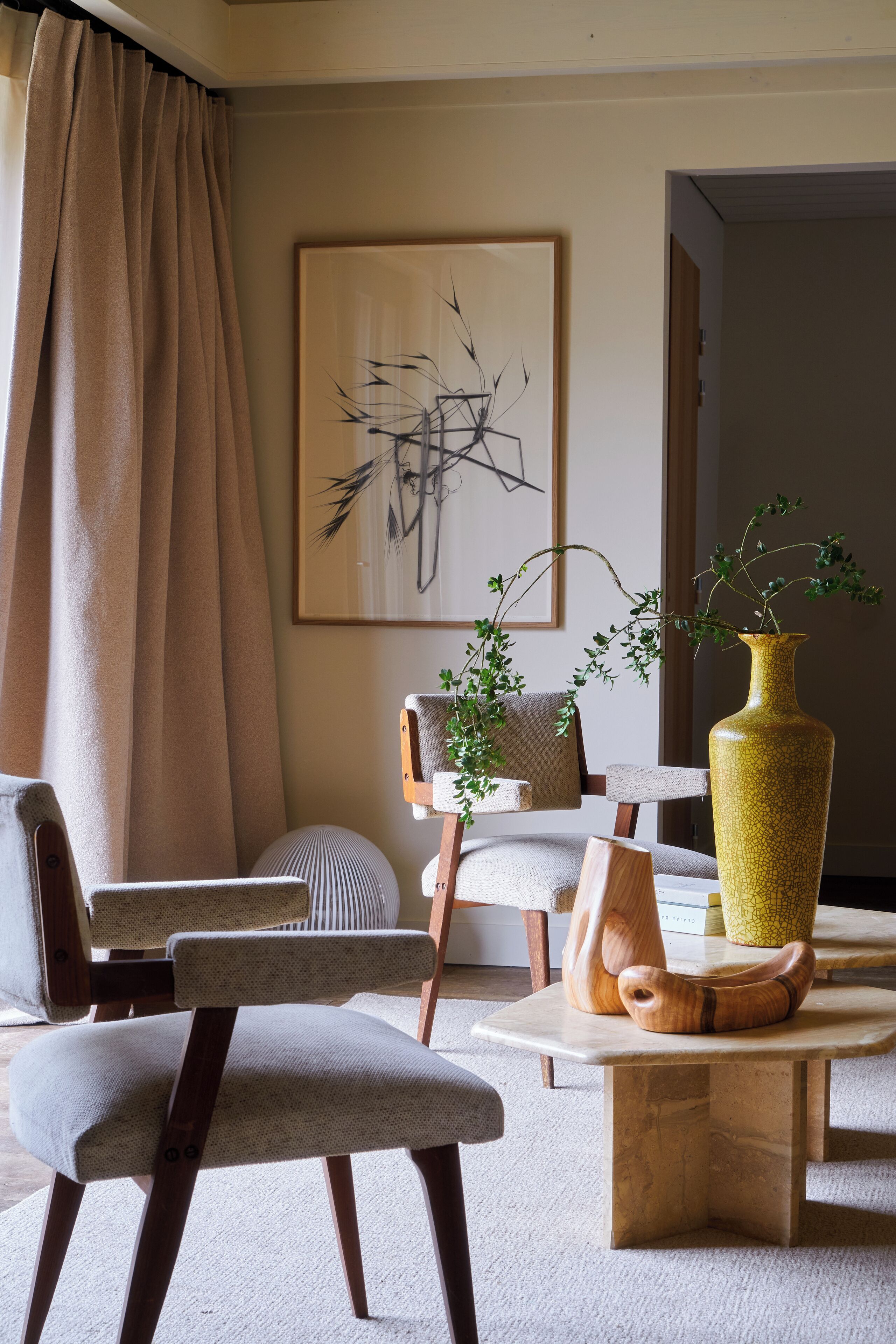 A modern living room with a sofa, armchair, and coffee table. There is a painting on the wall and a vase with plants on the table.
