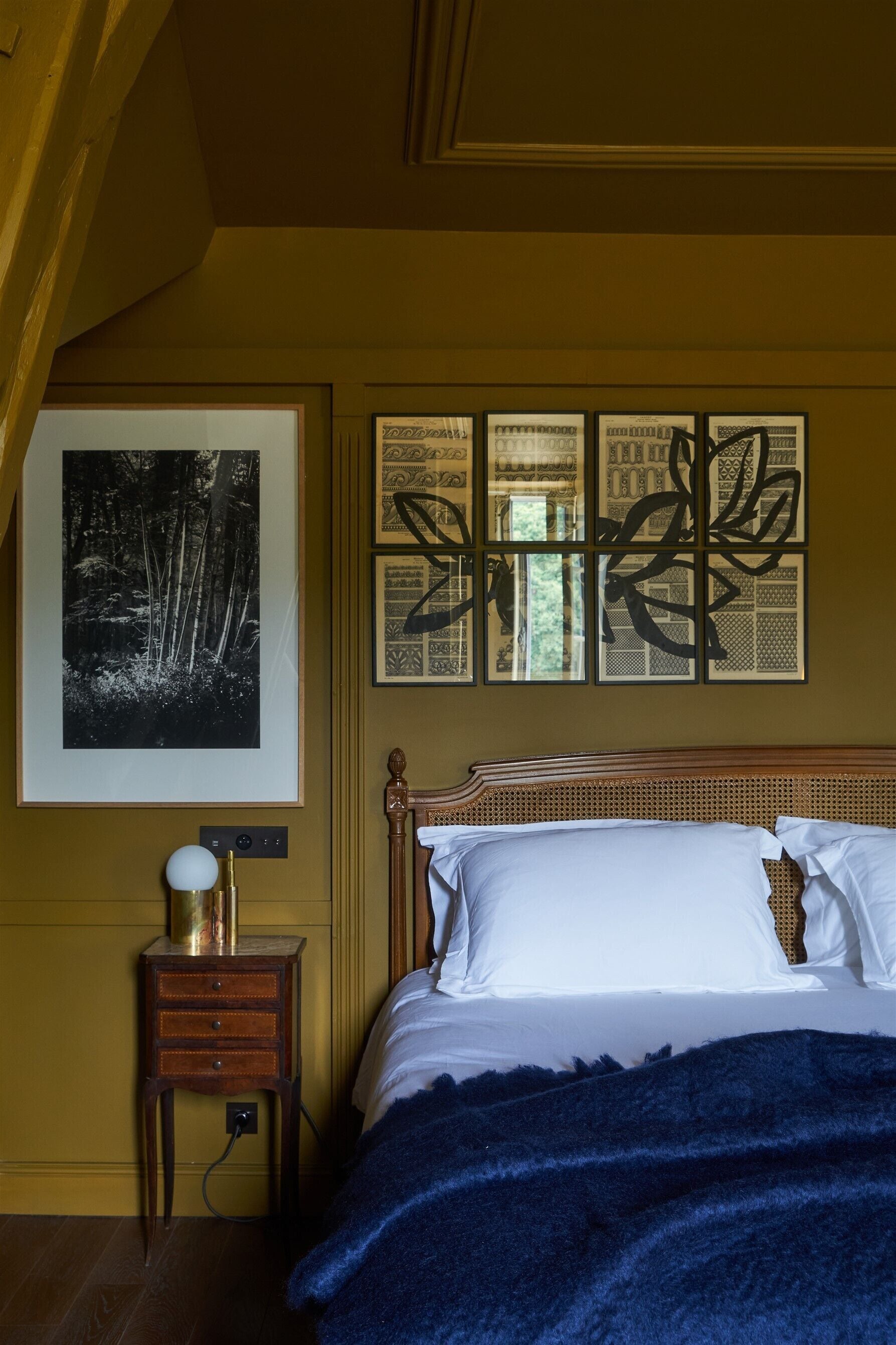 A bedroom with a bed, a nightstand, a lamp, and wall art.