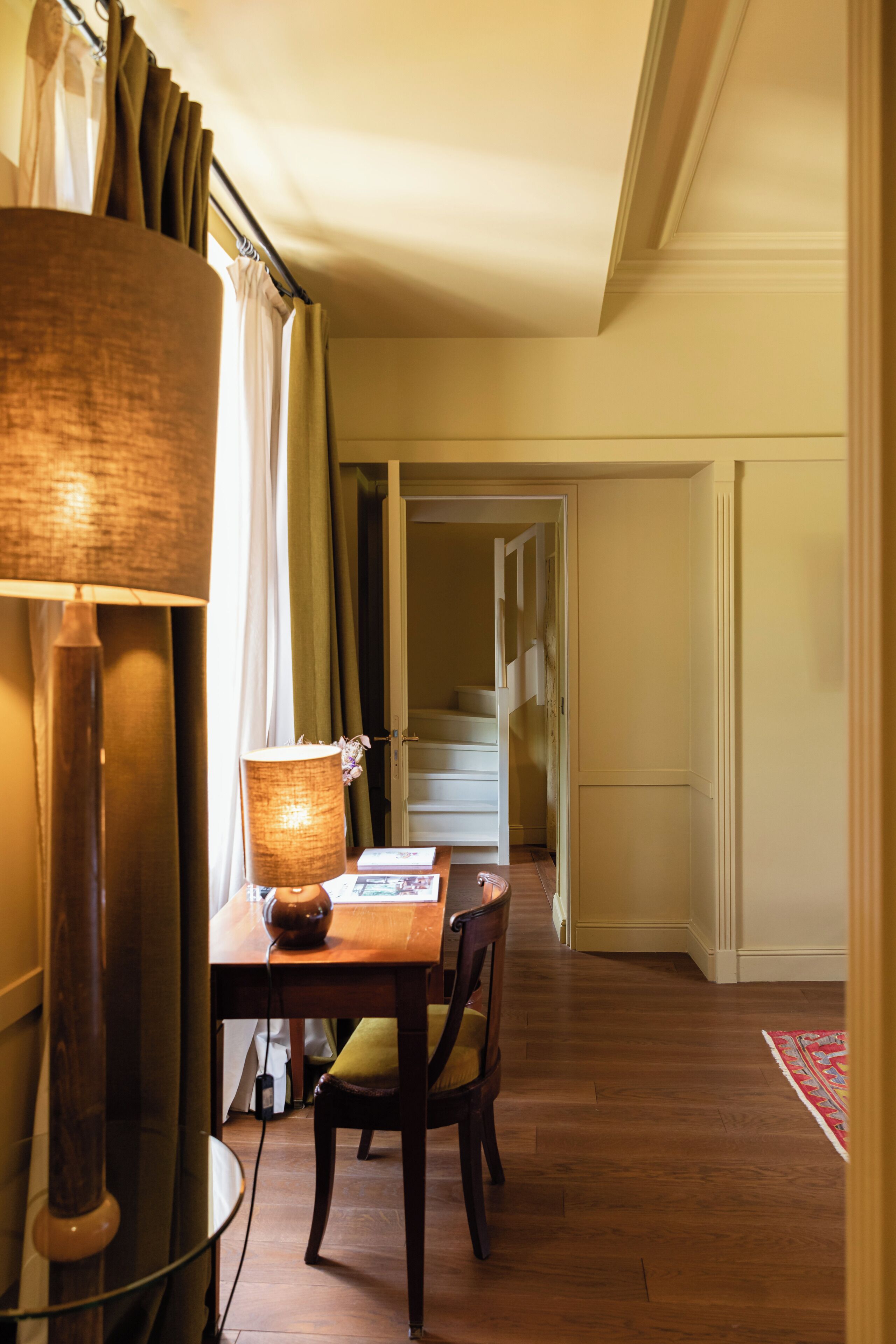 Un pasillo con suelo de madera, una mesa de comedor con sillas, una lámpara y una puerta que da a otra habitación.