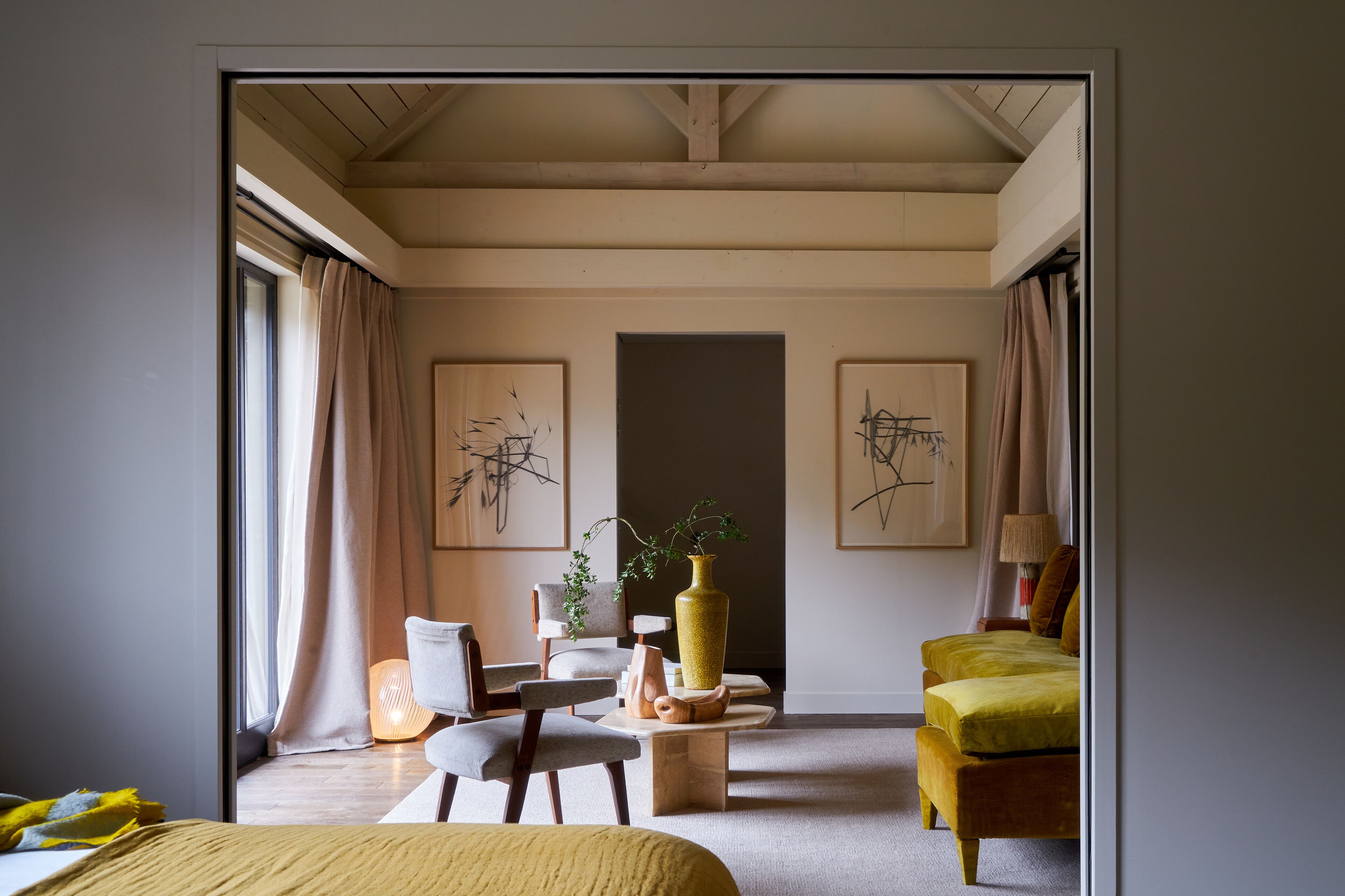 Una habitación de hotel moderna con una cama, un sillón amarillo, una mesita con un jarrón y obras de arte en las paredes.