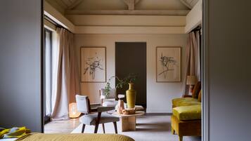 Una habitación de hotel moderna con una cama, un sillón amarillo, una mesita con un jarrón y obras de arte en las paredes.