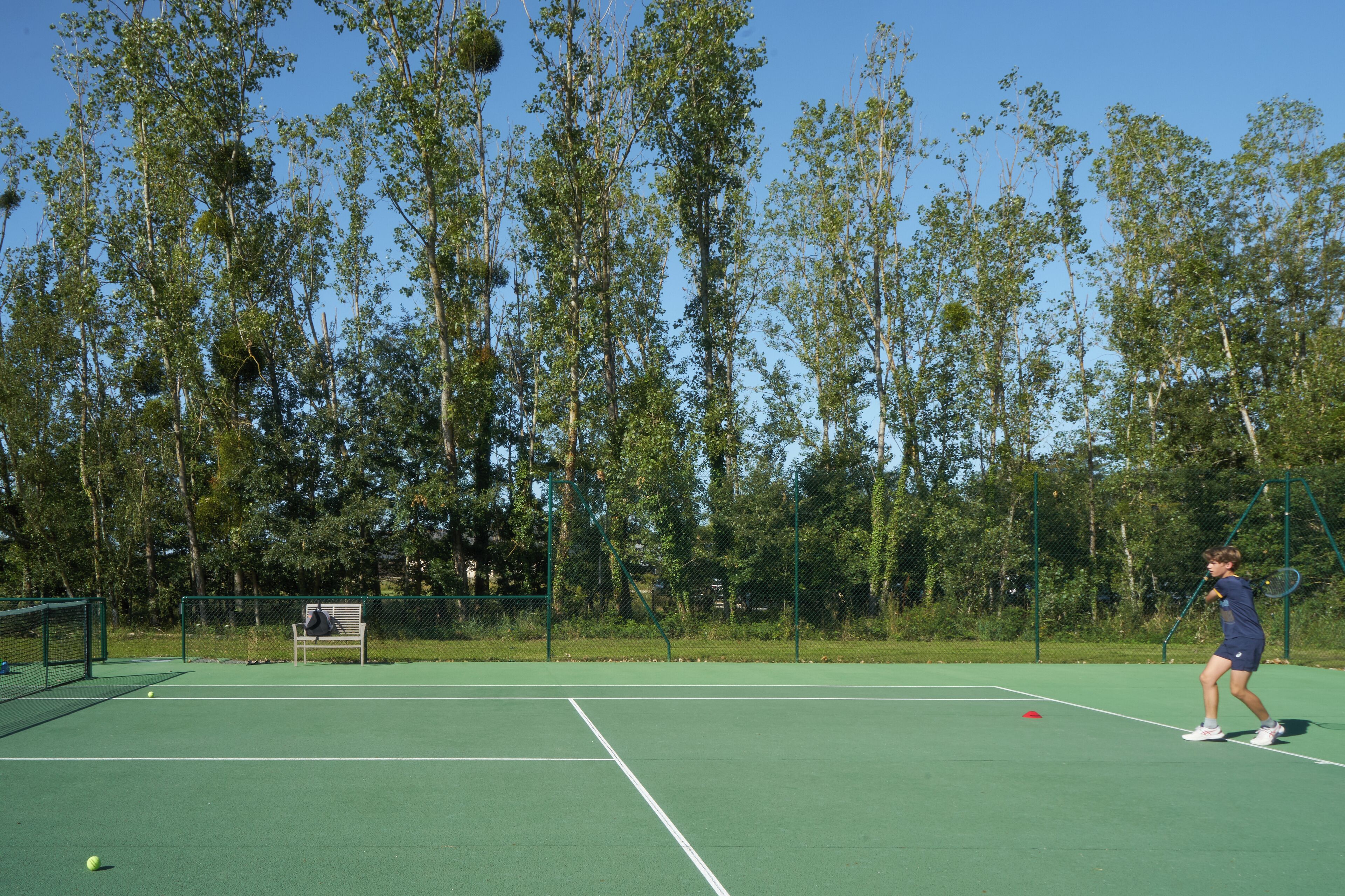 A tennis court with a net, a chair, and a fence.
