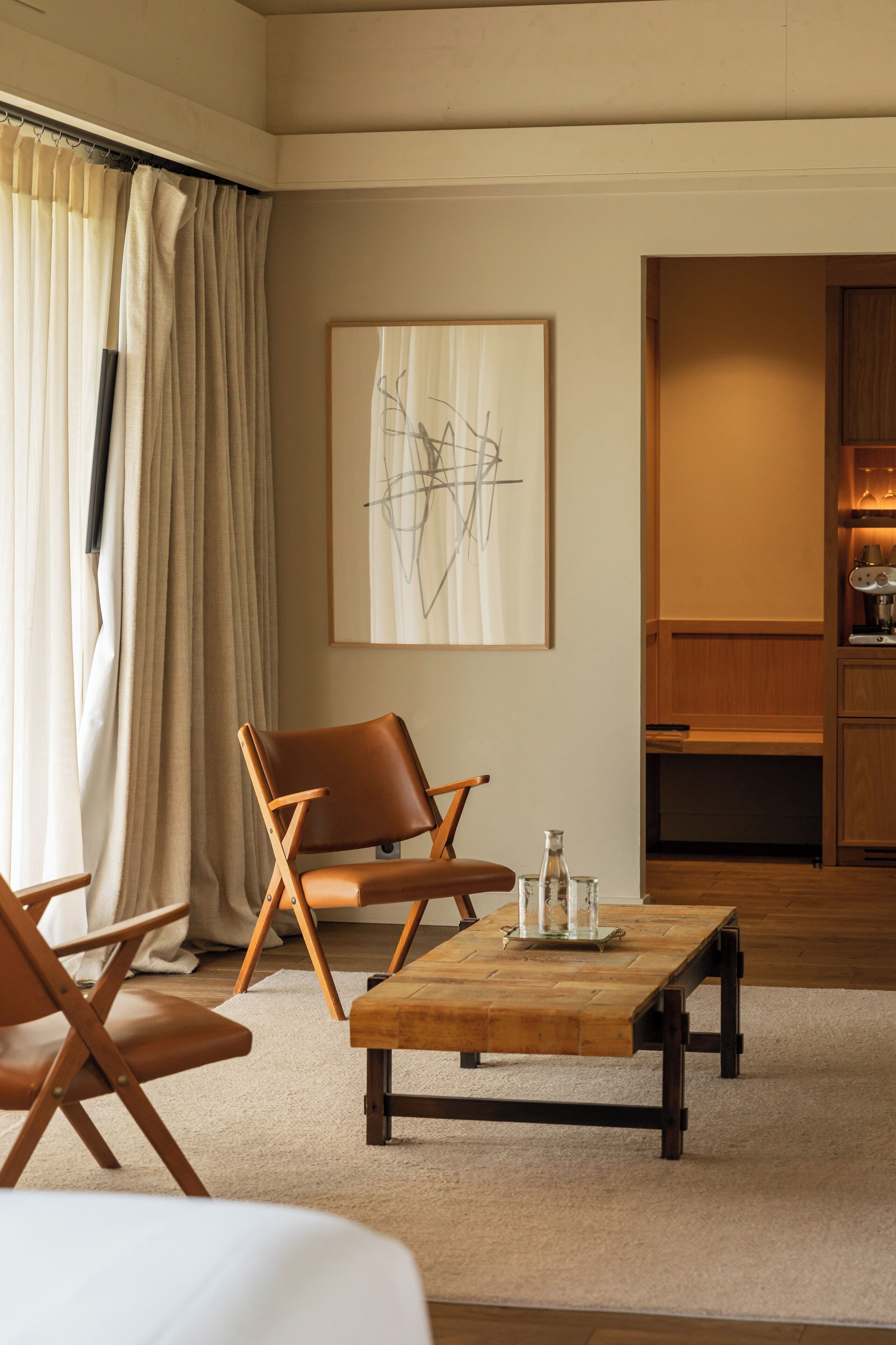 A modern living room with a wooden coffee table, leather armchairs, and a large abstract painting on the wall.
