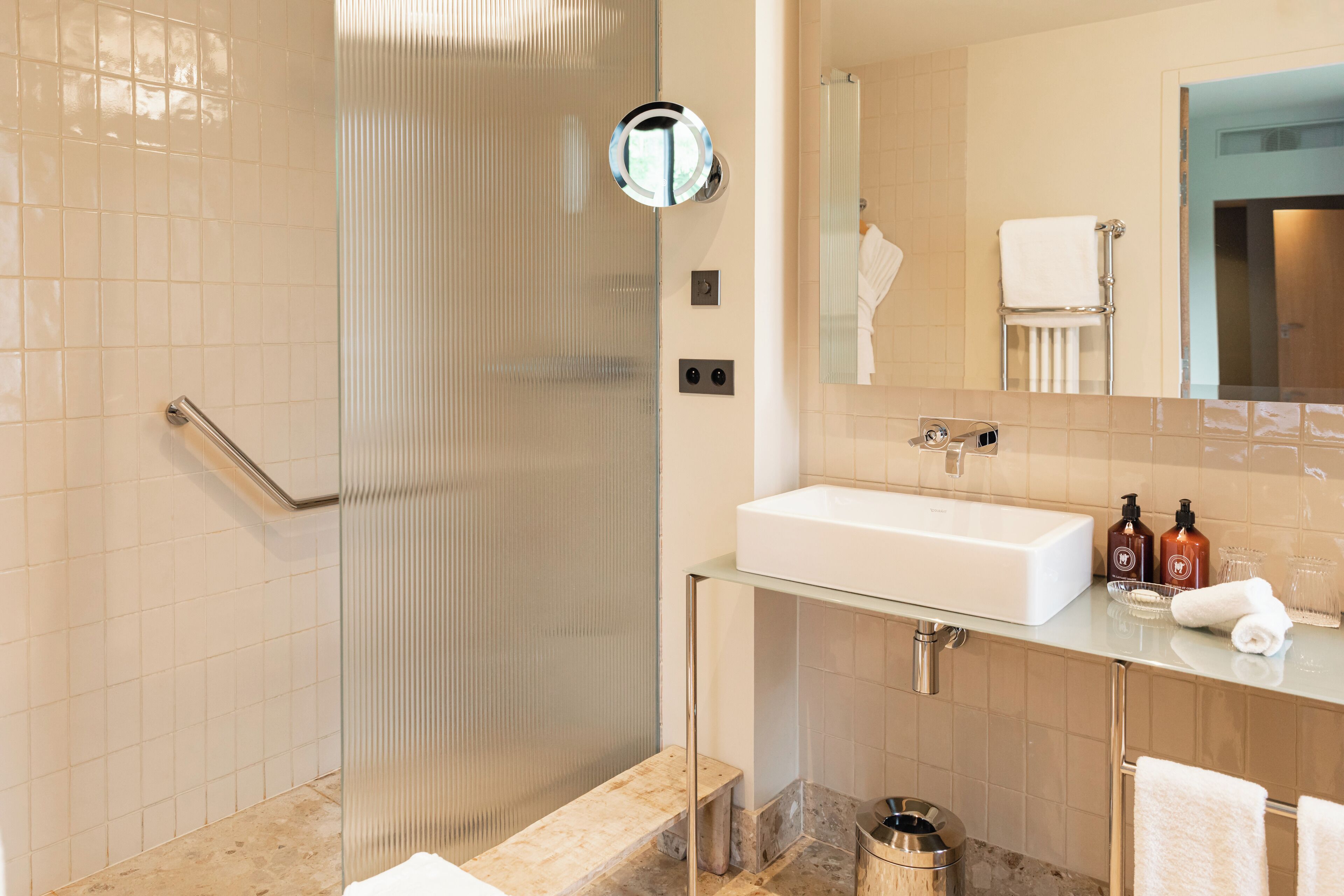 A modern bathroom with a glass shower enclosure, a white sink, and a vanity with toiletries.