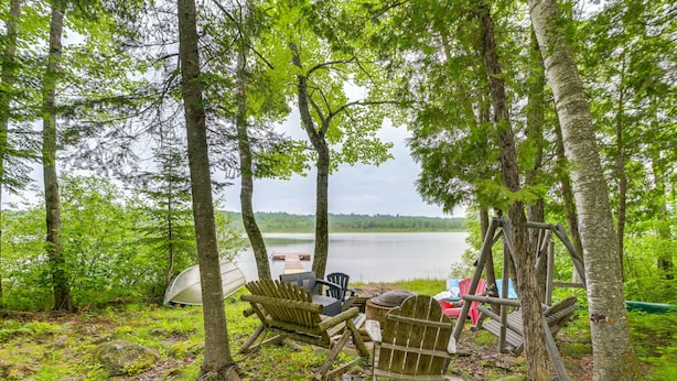 A rustic outdoor seating area with Adirondack chairs and a wooden deck overlooking a lake. - Near Snowmobiling: Secluded Harmony Cabin w/ Deck! (Harmony)