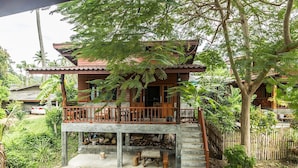 Ein zweistöckiges Holzhaus mit Balkon, umgeben von üppiger Vegetation und einem Holzzaun.