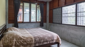 Ein Schlafzimmer mit Bett, großen Fenstern mit Vorhängen und Holzvertäfelung an den Wänden.