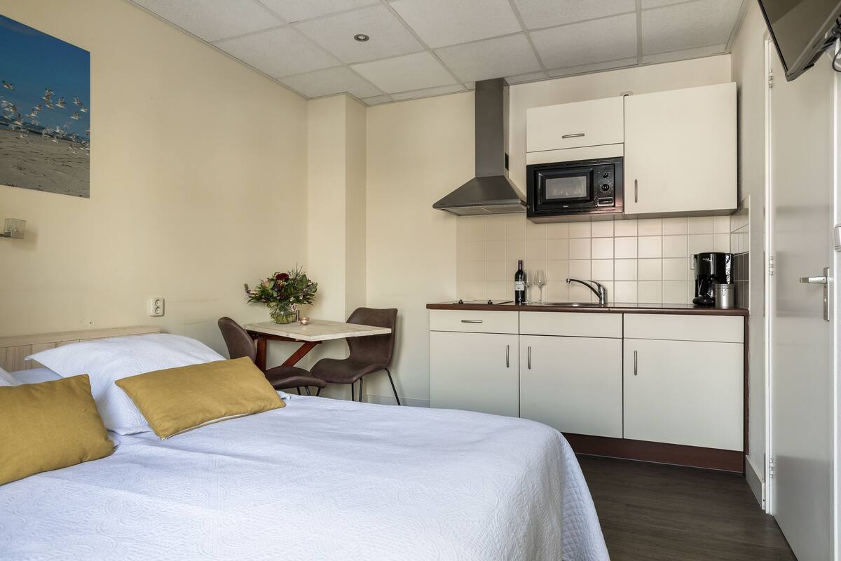 Una habitación de hotel compacta con una cama, una pequeña mesa de comedor, una silla, una kitchenette y un televisor montado en la pared.