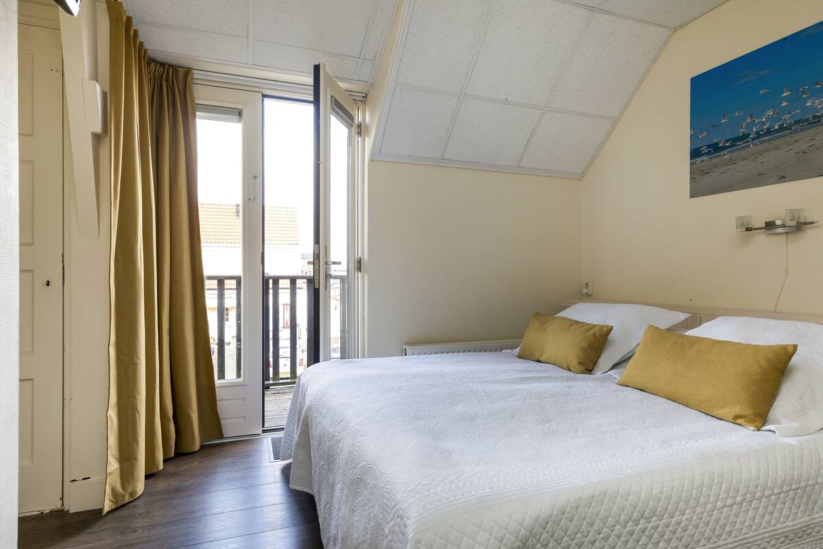 Un dormitorio con una cama, dos almohadas, una ventana con cortinas y un cuadro en la pared.