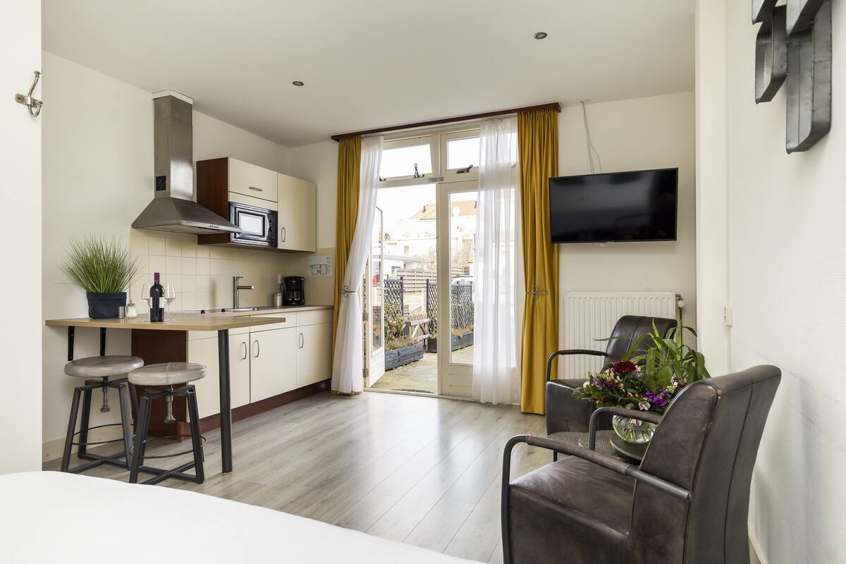Una cocina moderna con microondas, estufa y taburetes de bar. Hay una zona de comedor con mesa y sillas, y un televisor montado en la pared.