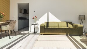 Un salon moderne comprenant un canapé, une table à manger avec des chaises, une petite table d’appoint avec un vase et un lampadaire.