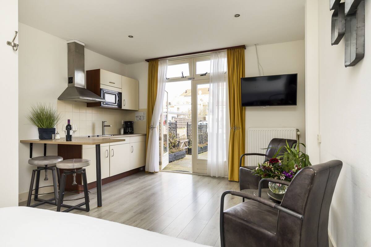 Una cocina moderna con microondas, estufa y taburetes de bar. Hay un comedor con mesa y sillas, y un televisor montado en la pared.