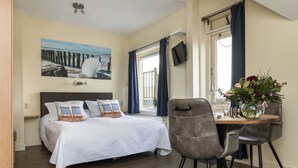 Une chambre à coucher avec un lit, un bureau avec des chaises, une télévision et une fenêtre avec des rideaux.