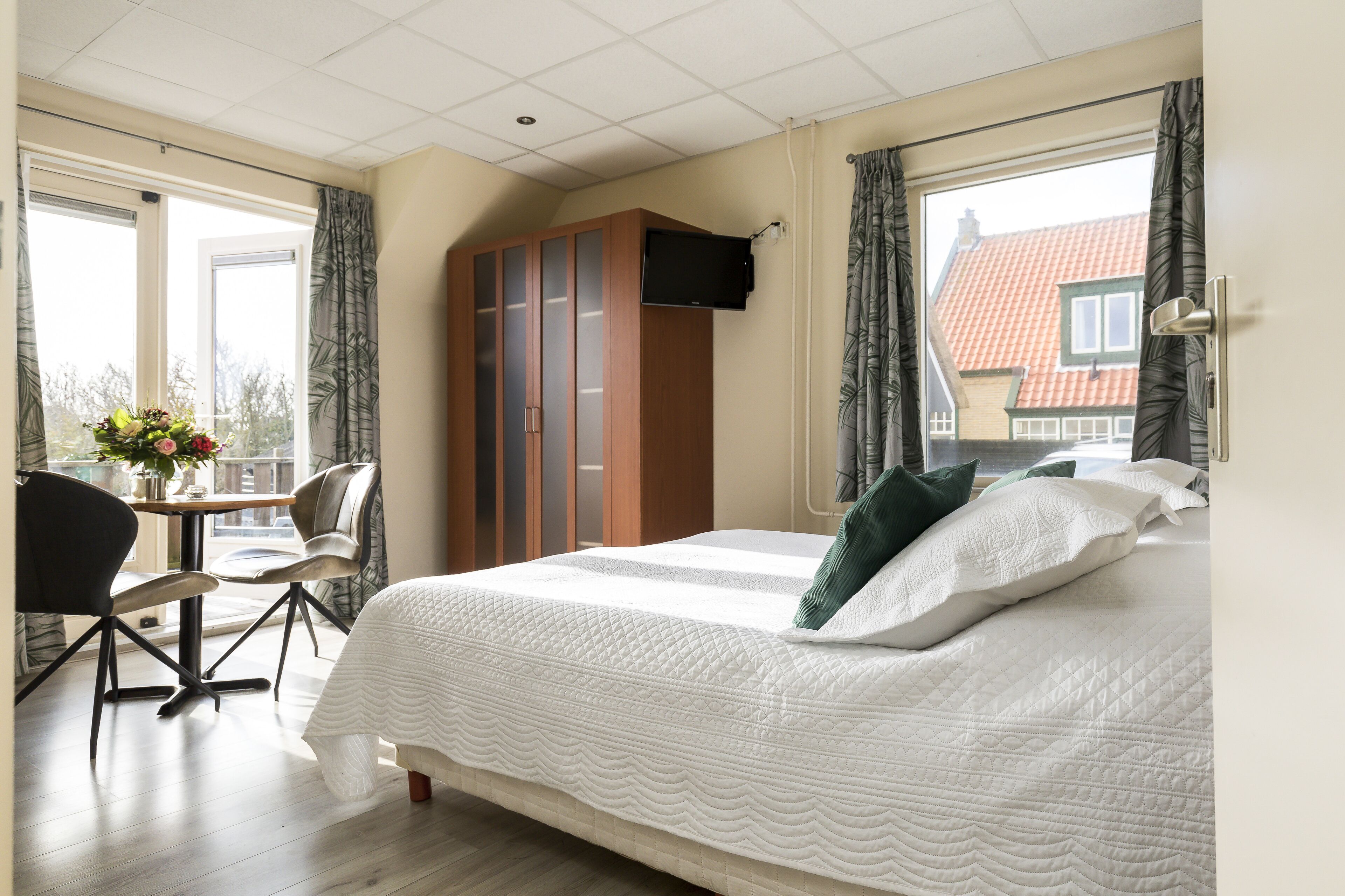 Une chambre d’hôtel avec un grand lit, un téléviseur fixé au mur, un bureau avec une chaise et une vue sur les bâtiments environnants.