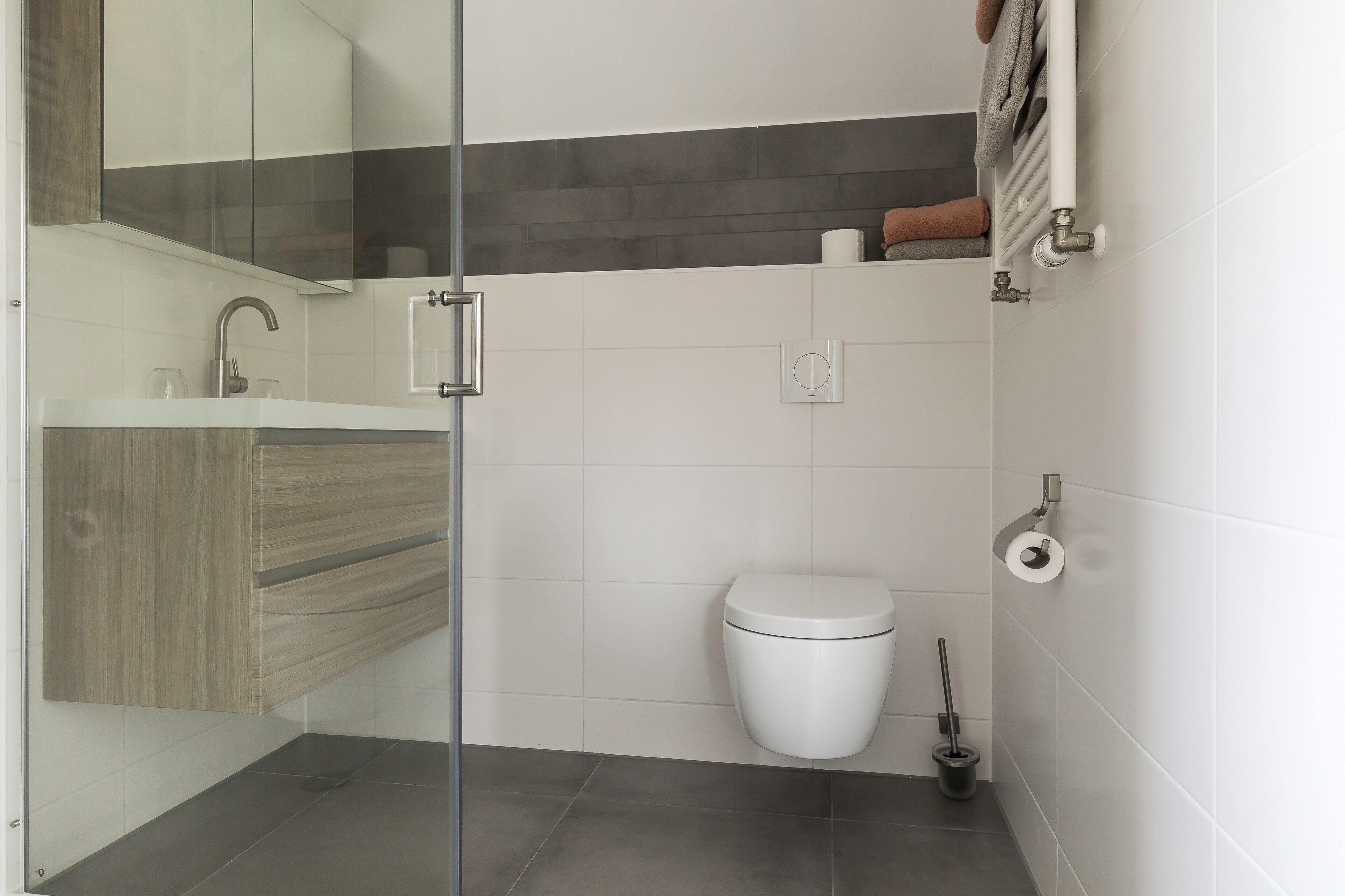 Une salle de bain moderne avec une douche à parois de verre, des toilettes blanches et un porte-serviettes.
