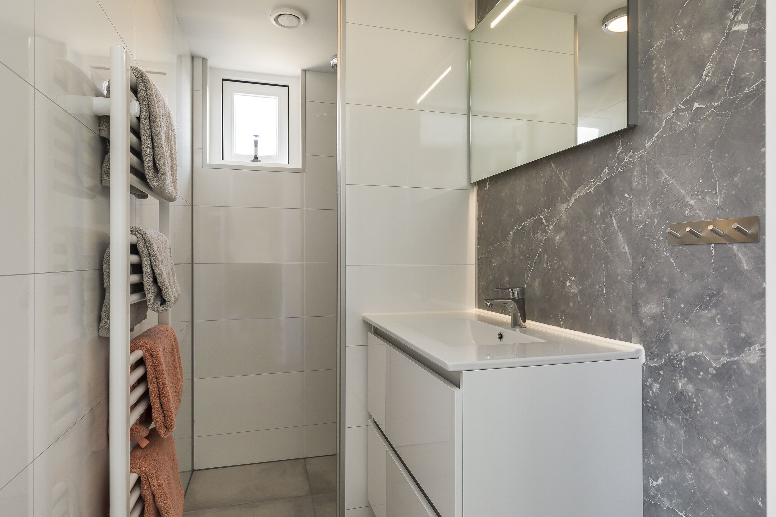 Un baño con un lavabo blanco, un espejo y un perchero con varias toallas.