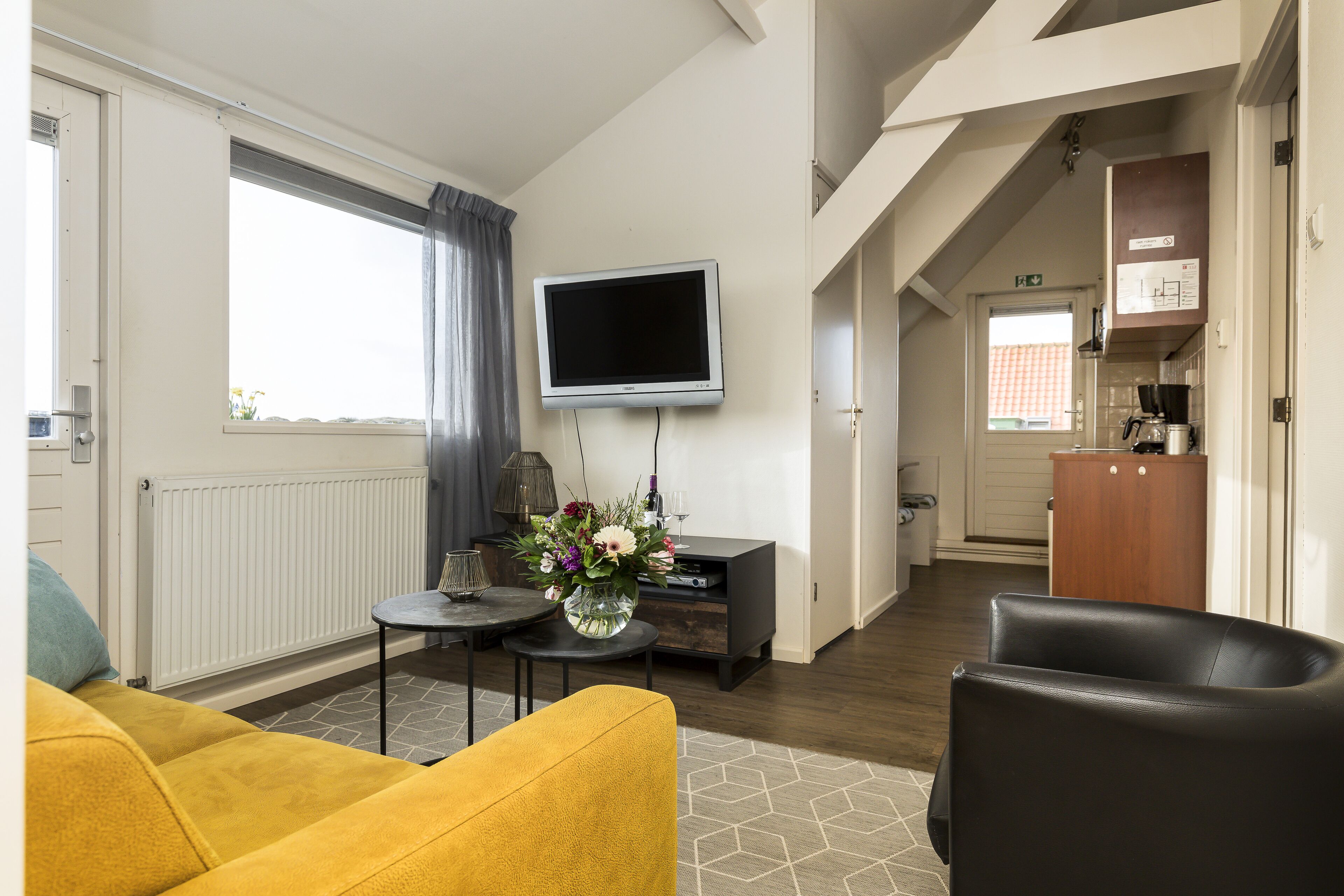 Un salon moderne avec un canapé, une table basse, un téléviseur à écran plat et un vase de fleurs.