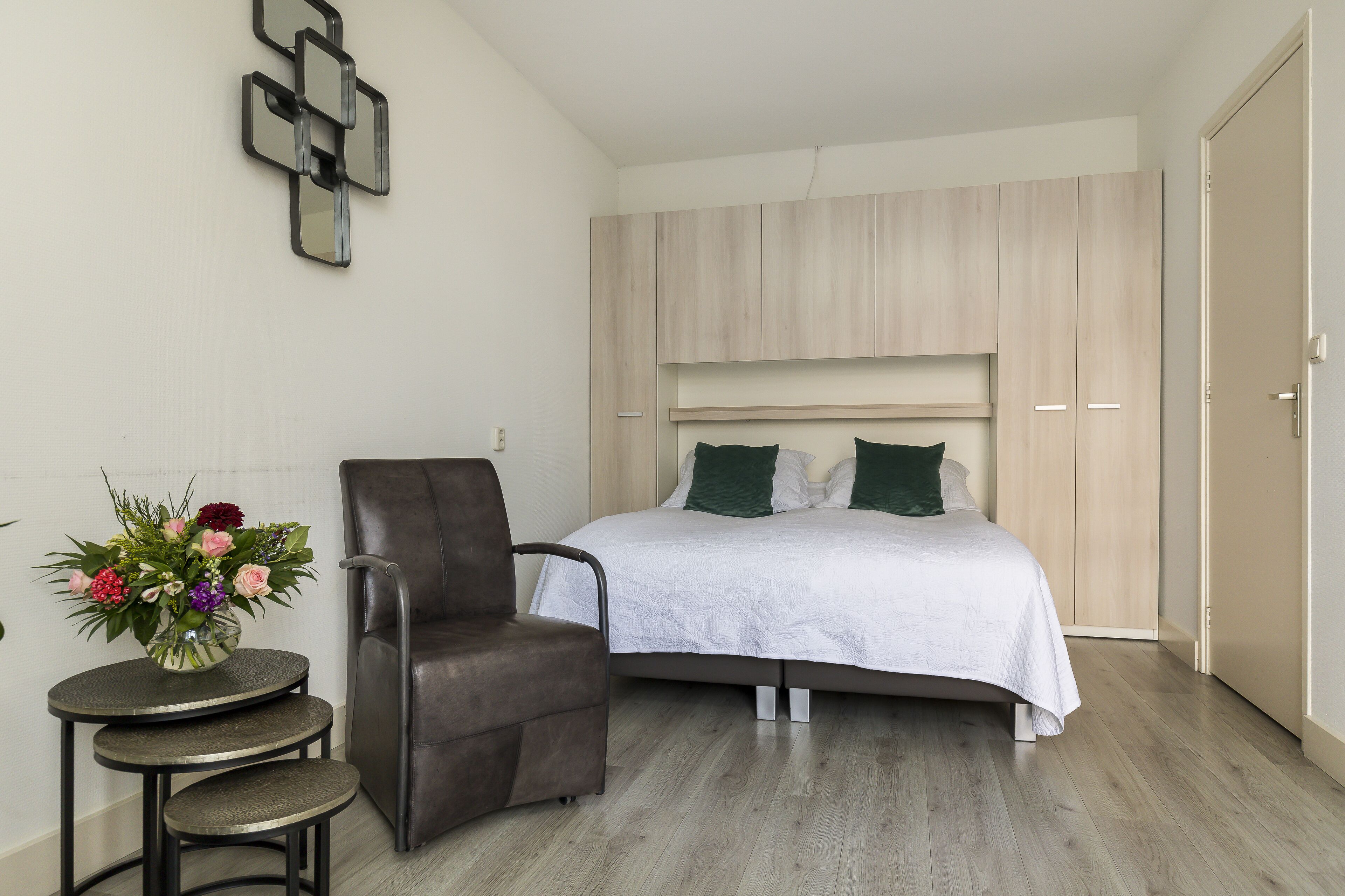 Un dormitorio con una cama, una silla, una mesita con un florero y un armario.
