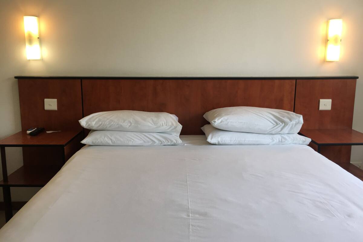 A hotel room with a large bed, two bedside tables, and wall-mounted lights.