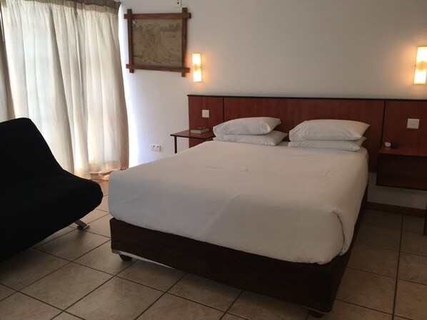 Una habitación de hotel con una cama grande, una mesita de noche, una silla y un cuadro en la pared.