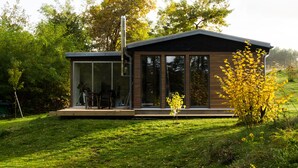 Ett modernt hus med en glasveranda, ett trädäck och en trädgård.