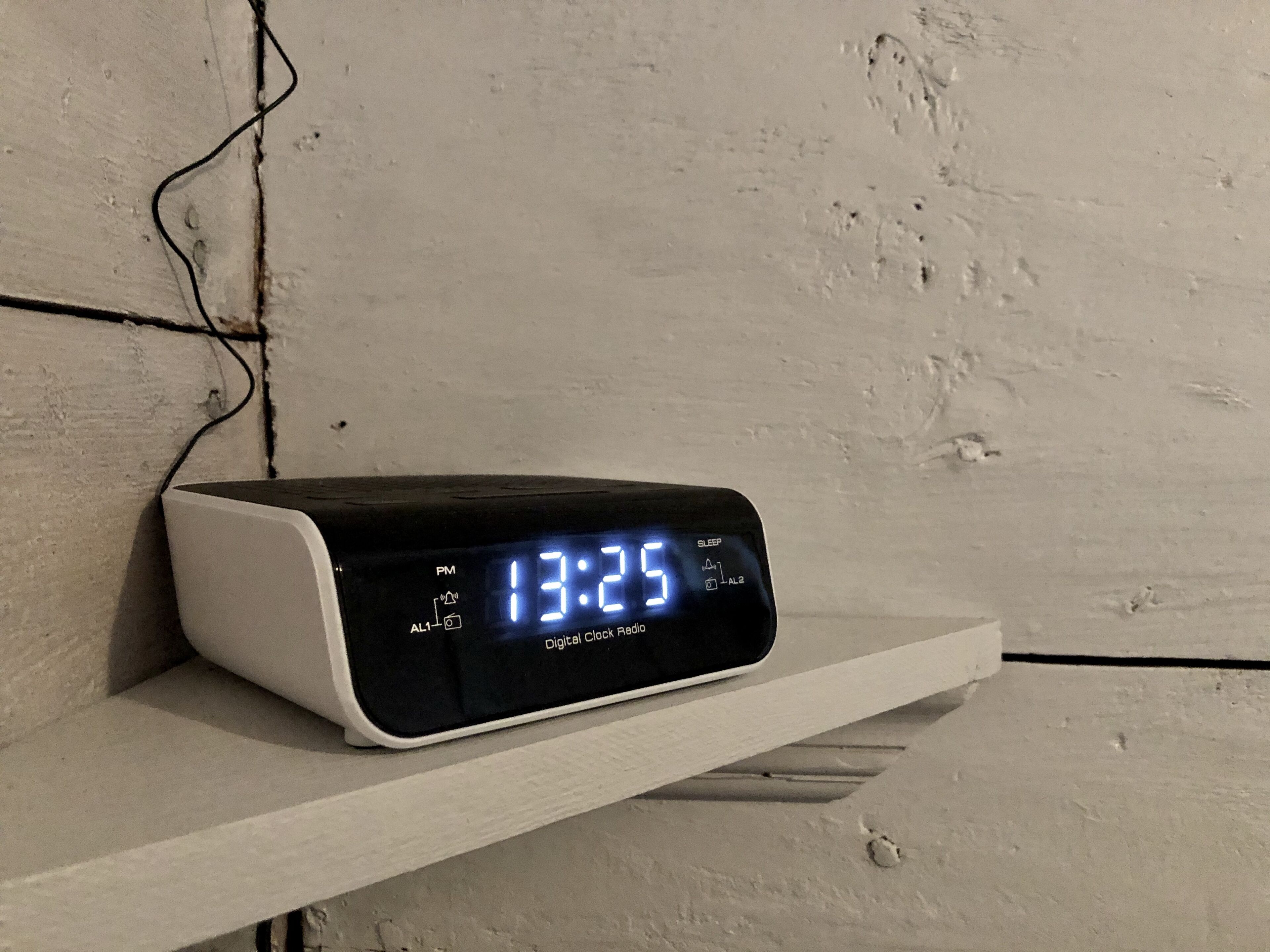 Um relógio digital numa prateleira branca em frente a uma parede texturizada.