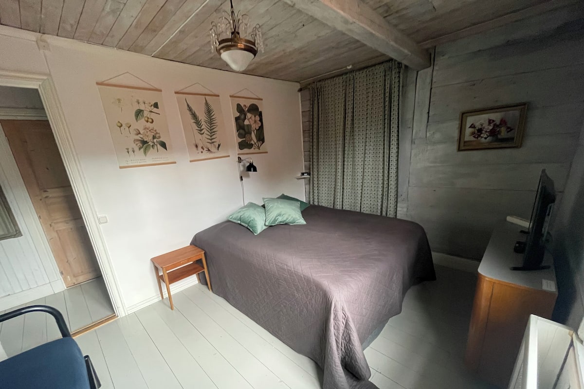 A bedroom with a bed, a small table, a desk with a computer, and a window with curtains.