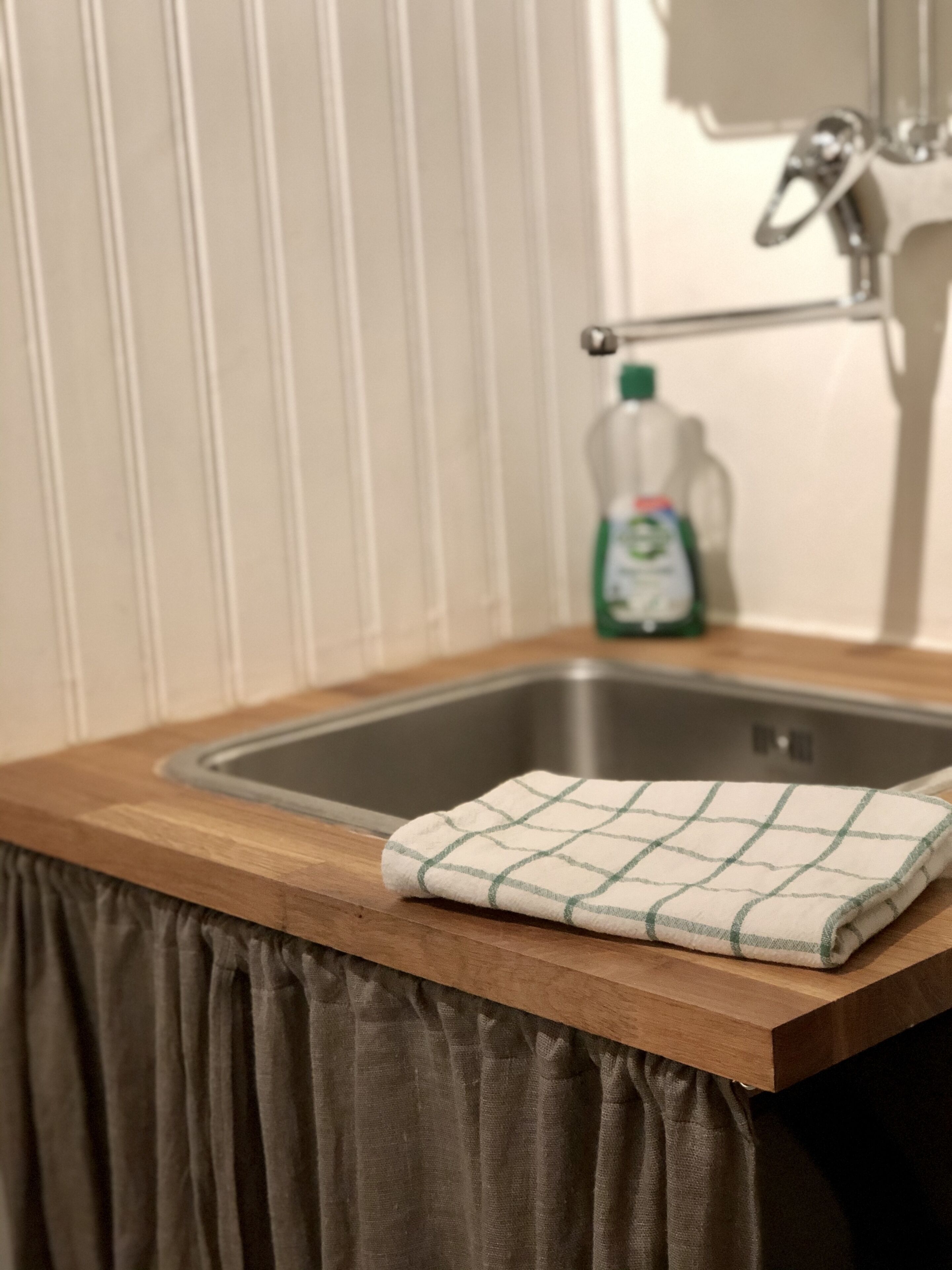 Una cocina con encimera de madera, un lavamanos de acero inoxidable y una botella verde de detergente.