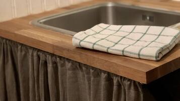 Una cocina con encimera de madera, un lavamanos de acero inoxidable y una botella verde de detergente.