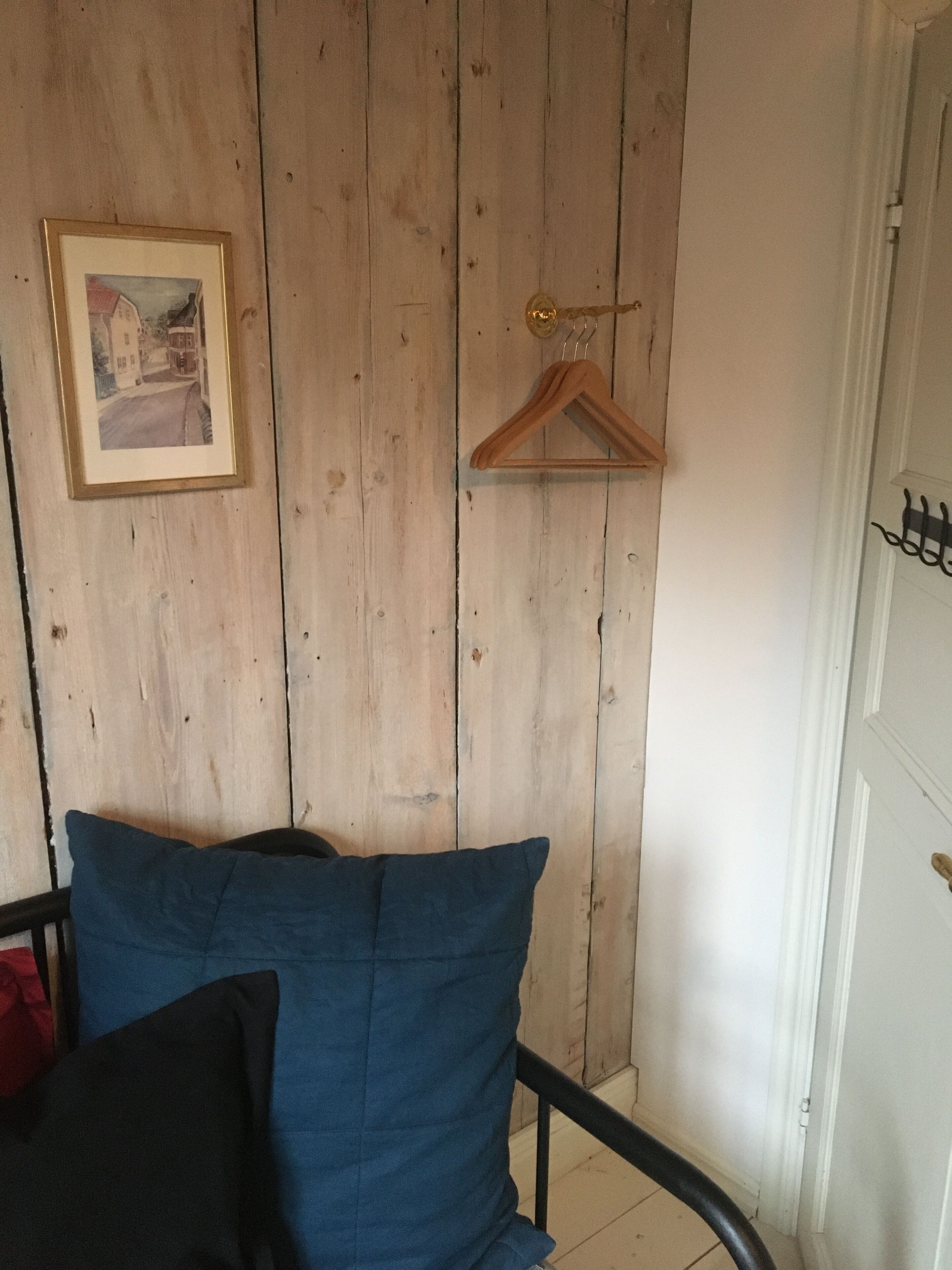 A room with a bed, a wooden wall, a door, and a framed picture.