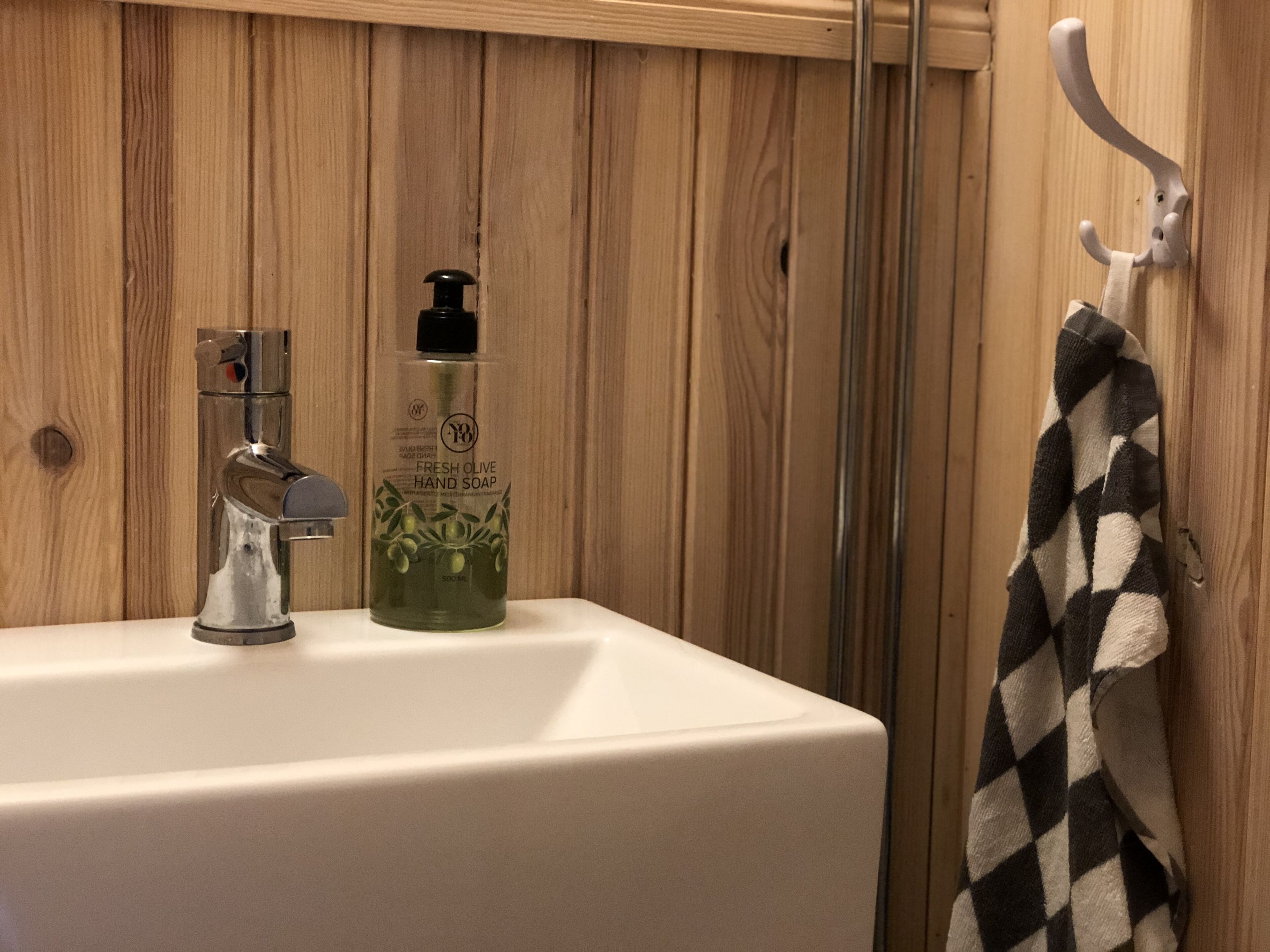 A bathroom with a white sink, a bottle of hand soap, and a towel hanging on a hook.