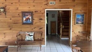 Un interior de madera con un banco, una mesa de comedor y sillas, una escalera y obras de arte enmarcadas en las paredes.