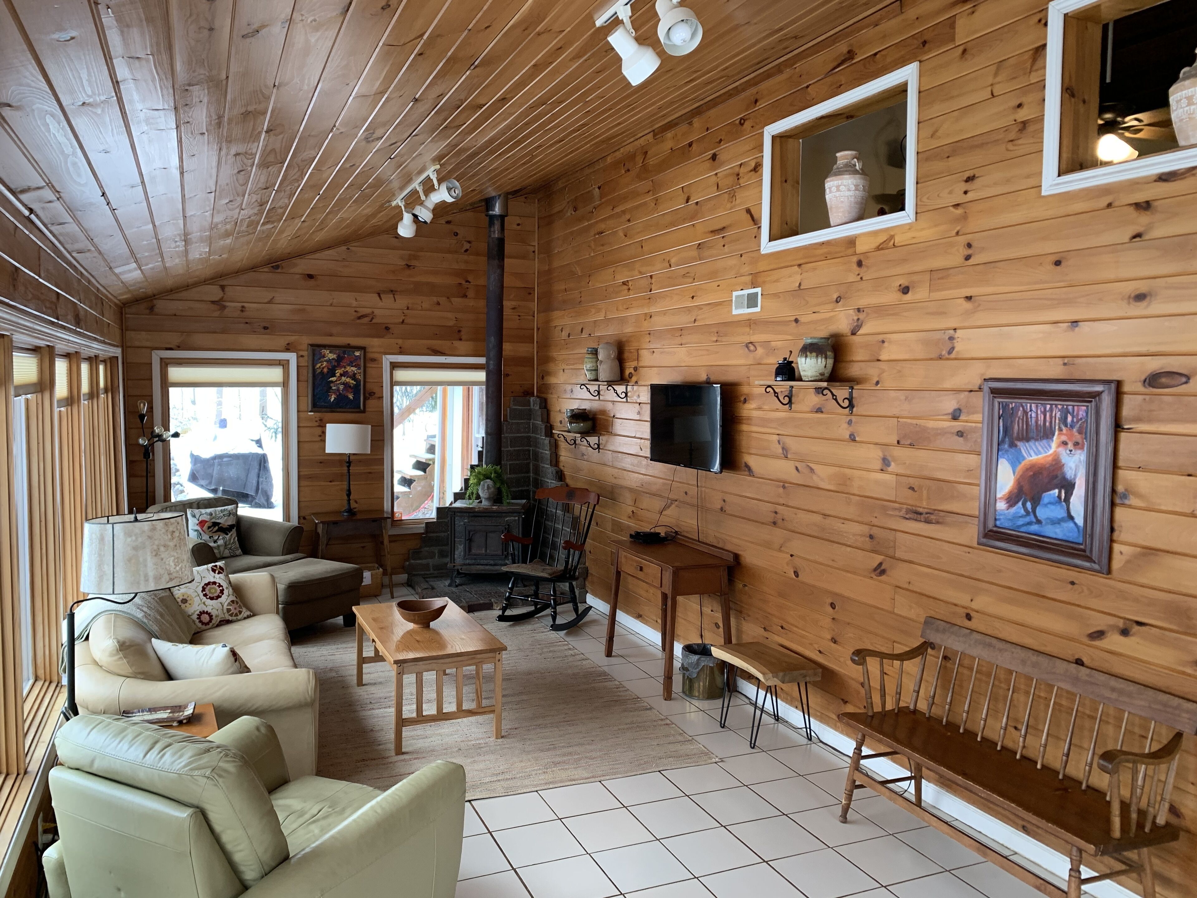 A cozy cabin interior with wooden walls, a fireplace, a television, and a fox painting.