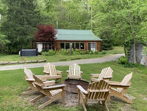 Una cabaña con techo verde rodeada de césped y cuatro sillas Adirondack de madera dispuestas alrededor de un brasero.