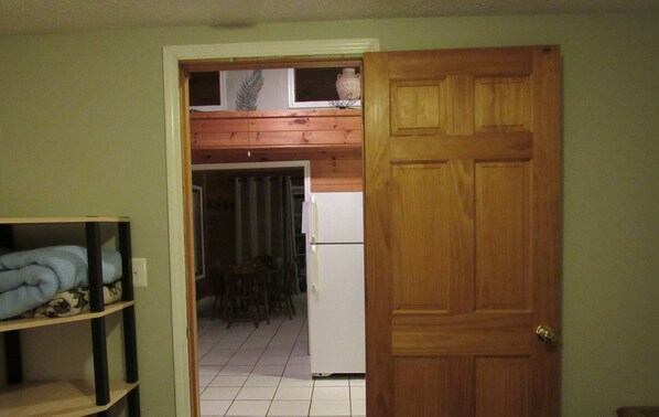 Una habitación con puerta de madera, refrigerador blanco y piso de baldosas.