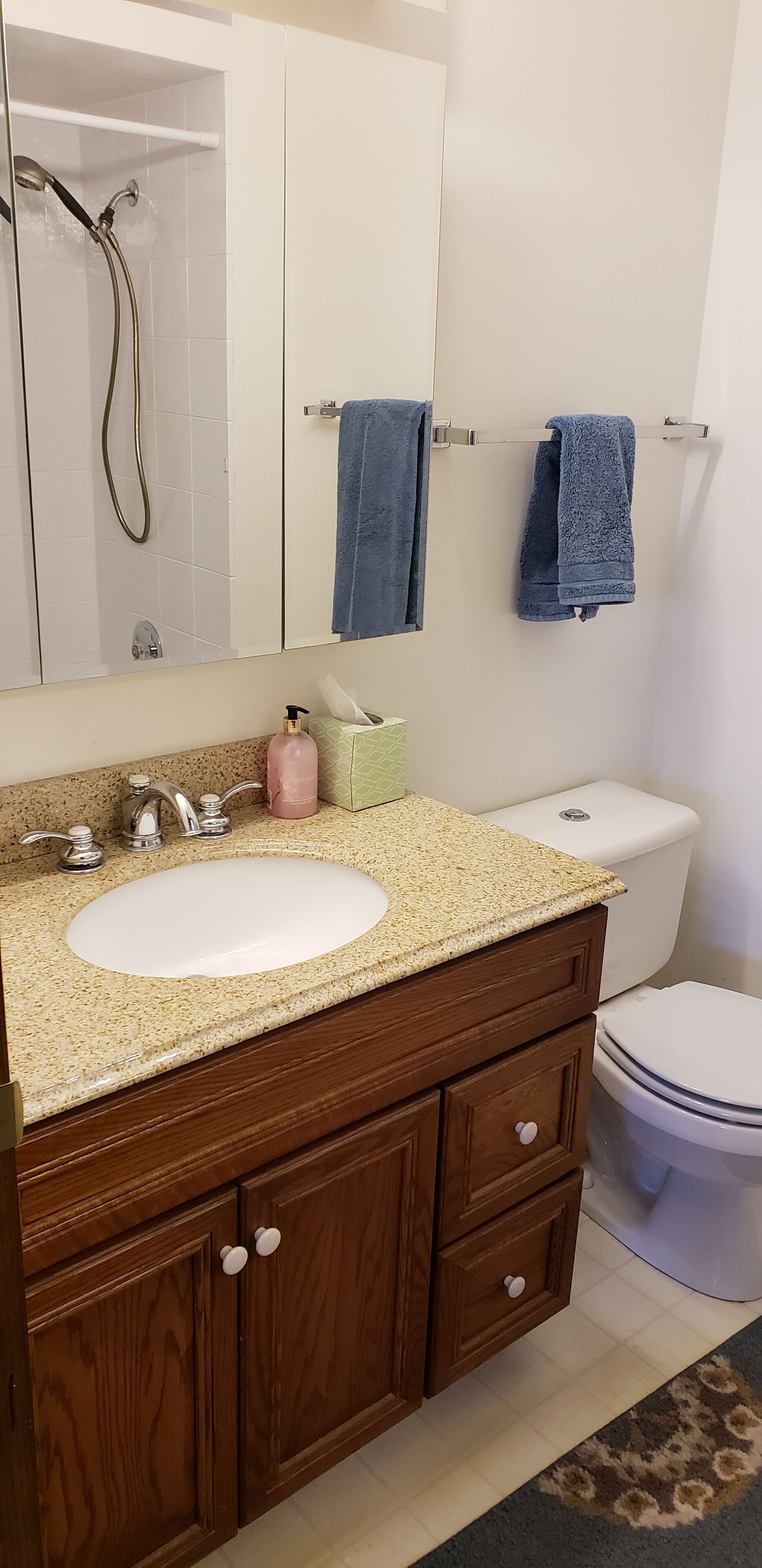 A bathroom with a white sink, wooden vanity, a mirror, a towel rack with two towels, and a toilet.